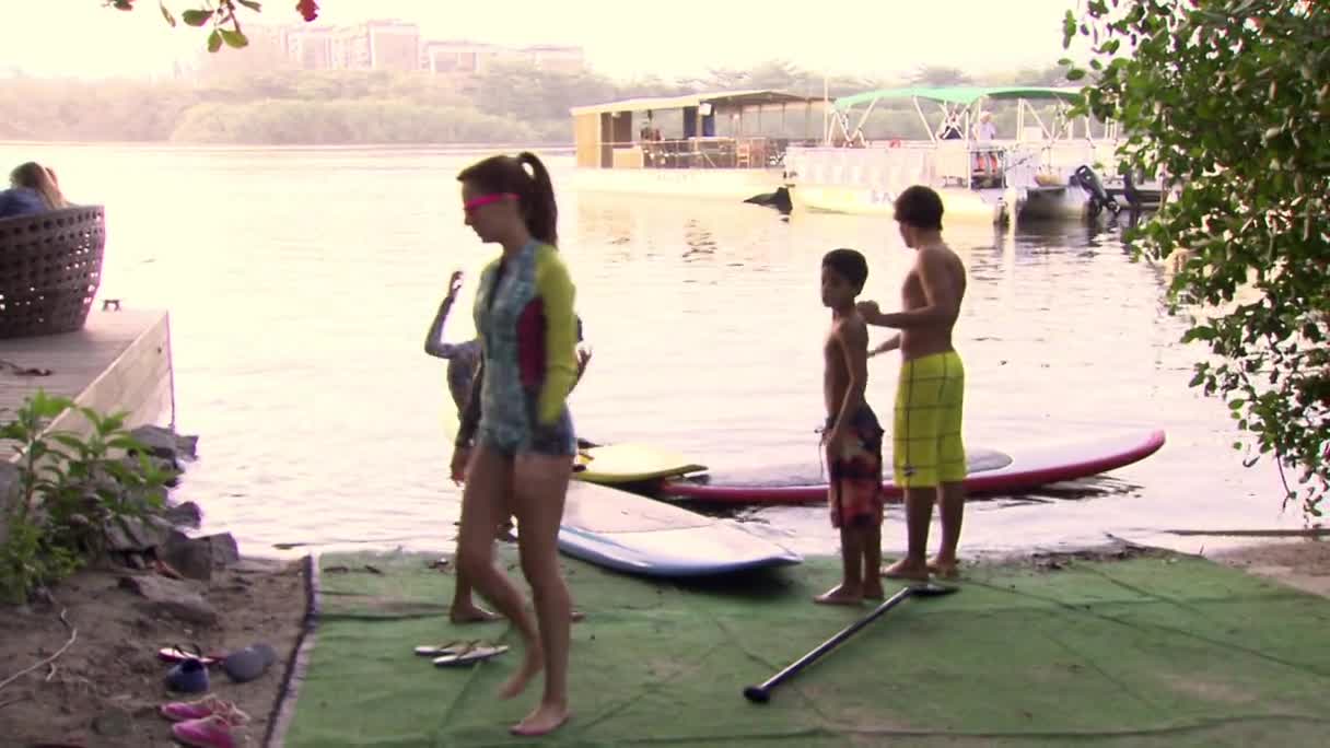 A young woman in a colorful swimsuit, blindfolded, is being guided by a boy. Another boy stands nearby, ready to help. A young woman in a colorful swimsuit, blindfolded, is being guided by a boy. Another boy stands nearby, ready to help.