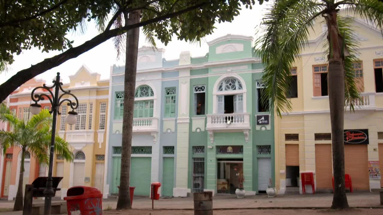 The pastel buildings of this Brazilian town stand in a row, their ornate balconies and arched windows catching the afternoon sun. A lone red trash can sits near a lamppost, its bright color a stark contrast to the muted tones of the street. The pastel buildings of this Brazilian town stand in a row, their ornate balconies and arched windows catching the afternoon sun. A lone red trash can sits near a lamppost, its bright color a stark contrast to the muted tones of the street.