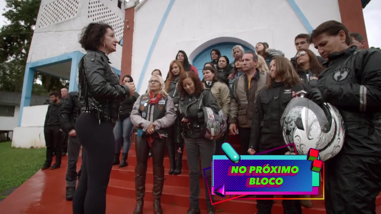 A group of people, many in motorcycle gear, stand on red steps outside a building. A woman in a black leather jacket addresses them, her voice clear and confident. A group of people, many in motorcycle gear, stand on red steps outside a building. A woman in a black leather jacket addresses them, her voice clear and confident.