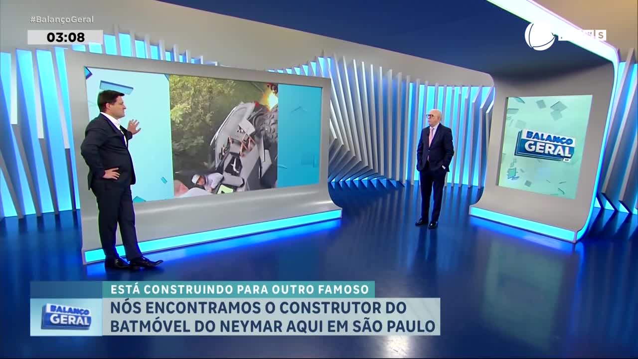 On the set of Brazil's Record News, a presenter gestures toward a screen showing a vehicle, while another man in a suit stands nearby. The lower third of the screen announces a story about the Batmobile and Neymar.
