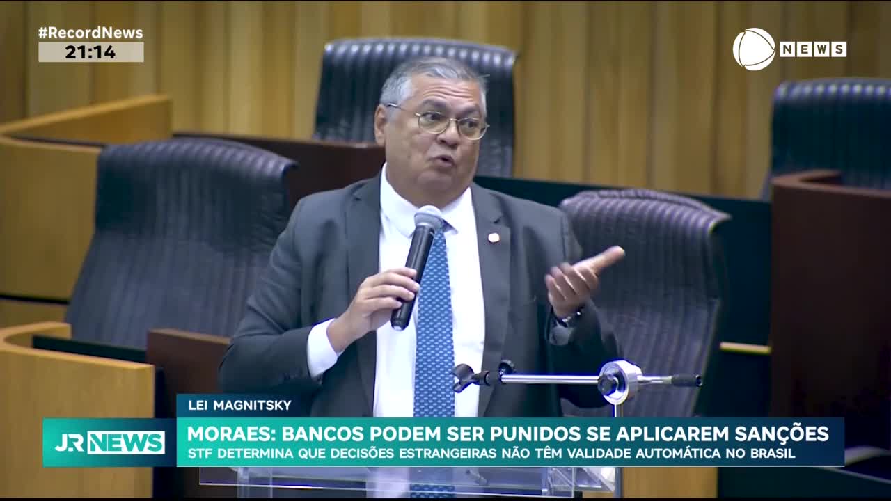 A man in a suit gestures emphatically, speaking into a microphone on a Brazilian news program. The Record News chyron at the top of the screen indicates the time is 21:14.
