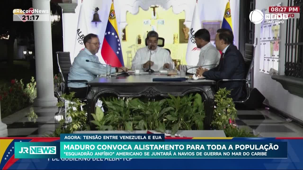 Maduro, flanked by others, speaks at a table, the Venezuelan flag visible behind him. The Record News logo and the time are displayed in the corner, with a headline about tension between Venezuela and the US.
