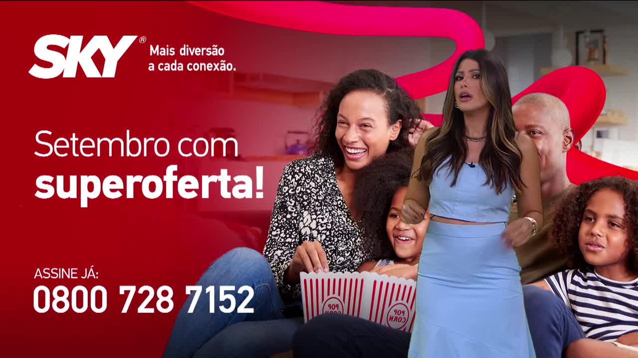 A woman in a blue outfit stands in front of a family, gesturing towards the camera. Beside them, a red banner advertises a September promotion from SKY, with a phone number to call in Brazil.
