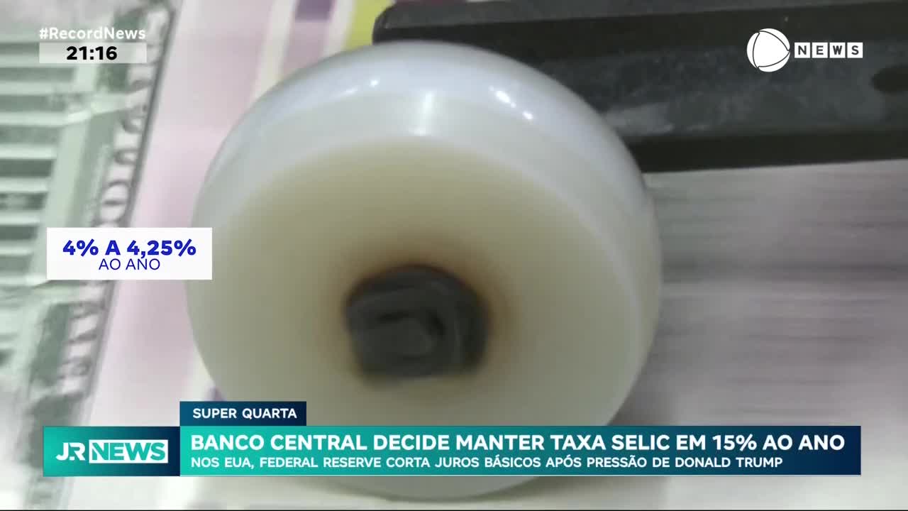 A close-up shows a white, cylindrical object with a dark center, likely a part of a machine. The Record News graphic displays financial information, with the headline mentioning the Banco Central and interest rates.
