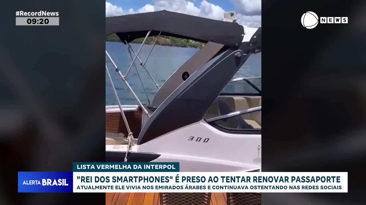 A white boat with a dark canopy sits still on the water, the "300" visible on its side. The Record News logo and a headline about a "Smartphone King" being arrested appear on the screen.
