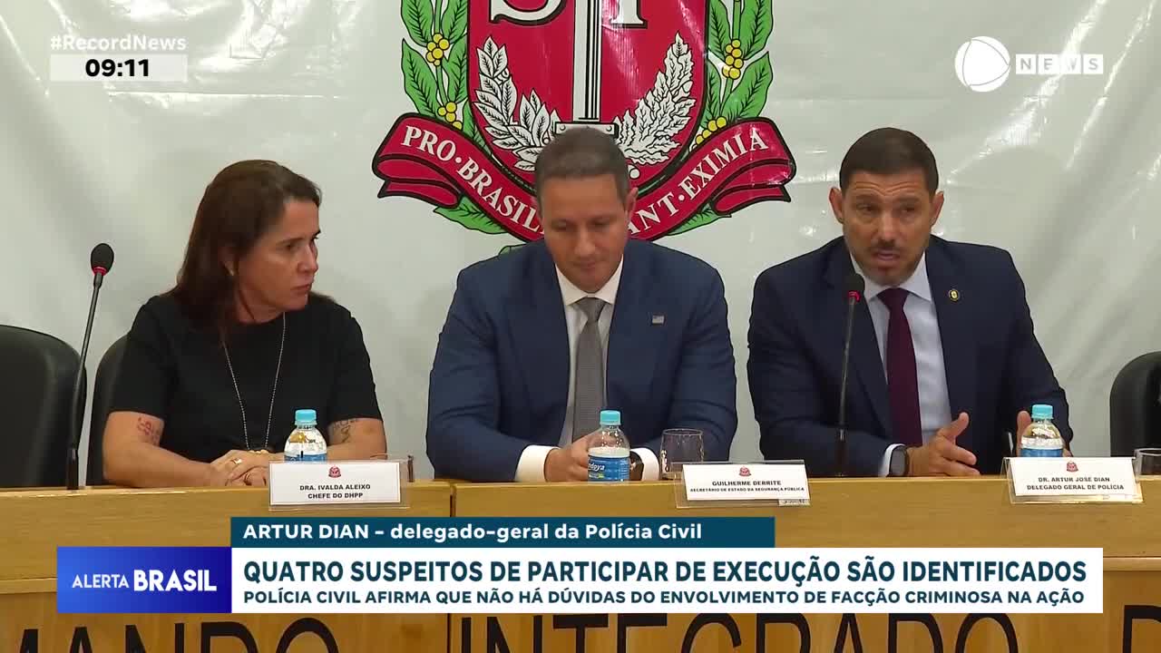 Three officials sit behind a table, speaking into microphones during a press conference on Record News in Brazil. The news ticker below announces the identification of suspects in an execution.
