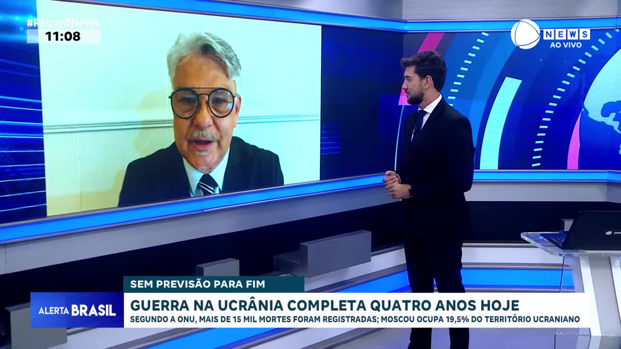 A man with gray hair and glasses speaks from a screen, while a news anchor in a suit stands nearby. The screen displays "Record News" and information about the war in Ukraine.