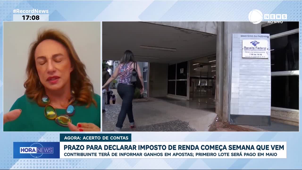 A woman in a patterned top and dark pants walks away from the camera toward the entrance of a building. She carries a dark handbag on her shoulder.