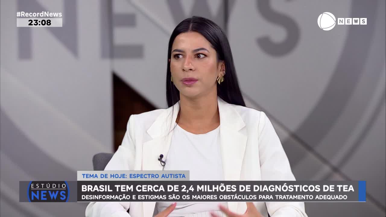 A woman in a white blazer speaks on a news program. The screen behind her displays "Record News" and the time, 23:08.