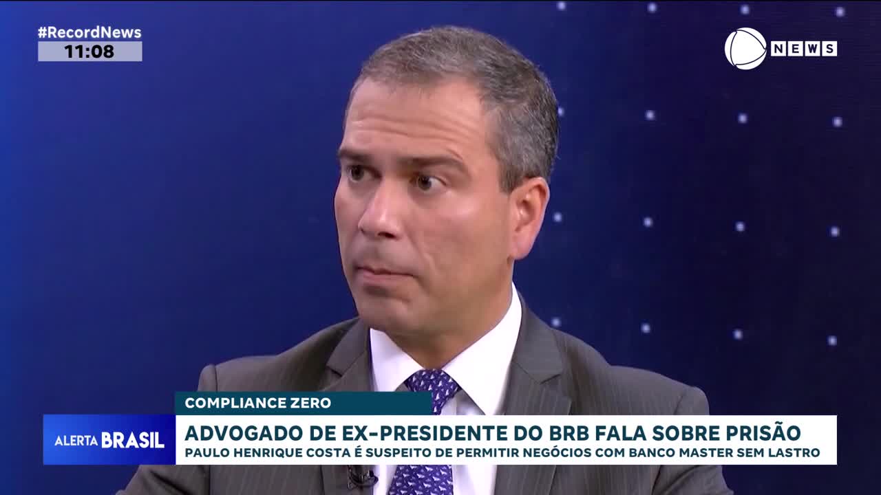 A man in a suit sits in front of a blue background with faint white dots. The Record News logo appears in the upper right corner. Text at the bottom of the screen indicates "Alerta Brasil" and discusses an attorney speaking about prison.
