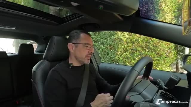 A man, wearing glasses and a black shirt, sits behind the wheel of a car, speaking. The camera, likely from Rede SPTV in Brazil, is positioned inside the vehicle, capturing his review.
