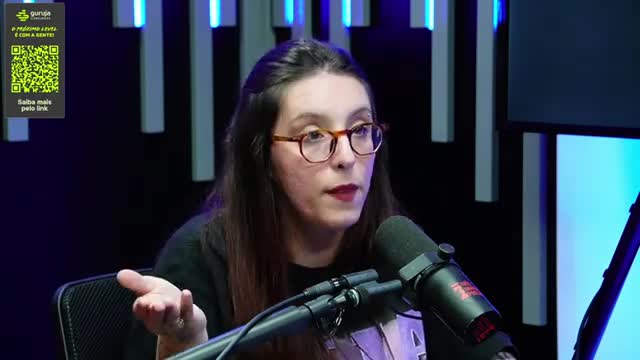 A woman with glasses gestures with her left hand as she speaks into a microphone. The background hints at a studio setting, possibly a broadcast from Brazil.
A woman with glasses gestures with her left hand as she speaks into a microphone. The background hints at a studio setting, possibly a broadcast from Brazil.
