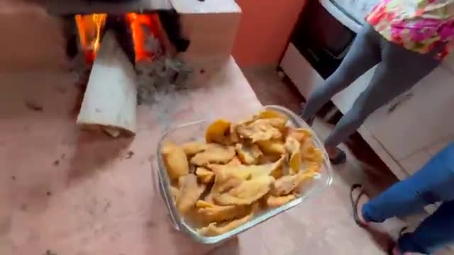 Flames lick at the wood in a brick stove, while a glass dish of fried food is held up. A person in the background appears to be reaching for the food.
Flames lick at the wood in a brick stove, while a glass dish of fried food is held up. A person in the background appears to be reaching for the food.