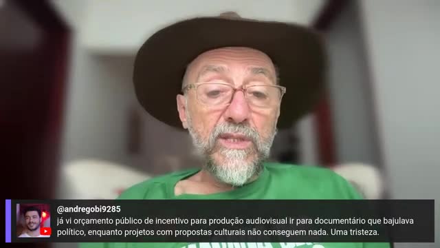 A man in a hat and glasses, wearing a green shirt, is speaking directly into the camera. Text from a viewer, likely on Rede SPTV in Brazil, appears below, commenting on public funding for documentaries.
A man in a hat and glasses, wearing a green shirt, is speaking directly into the camera. Text from a viewer, likely on Rede SPTV in Brazil, appears below, commenting on public funding for documentaries.