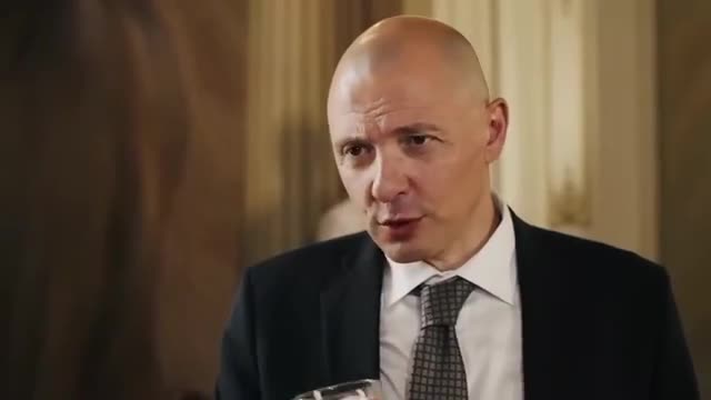 The man in the suit holds a glass, speaking directly to the camera. His expression is serious, and he seems to be in the middle of a discussion.
The man in the suit holds a glass, speaking directly to the camera. His expression is serious, and he seems to be in the middle of a discussion.