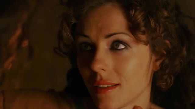 A woman with striking eyes and dark, curly hair leans in, her lips parted slightly as if about to speak. The dim lighting casts a warm glow, hinting at an intimate moment captured for Rede SPTV.