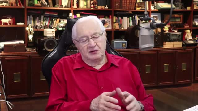 The man in the red shirt gestures with his hands as he speaks, his voice likely reaching listeners across Brazil via Rede SPTV. Shelves filled with books and vintage electronics surround him.