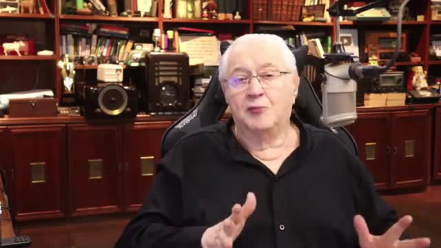A man in a black shirt speaks animatedly, his hands gesturing. Behind him, shelves overflow with books and vintage electronics, a scene familiar to Rede SPTV viewers.