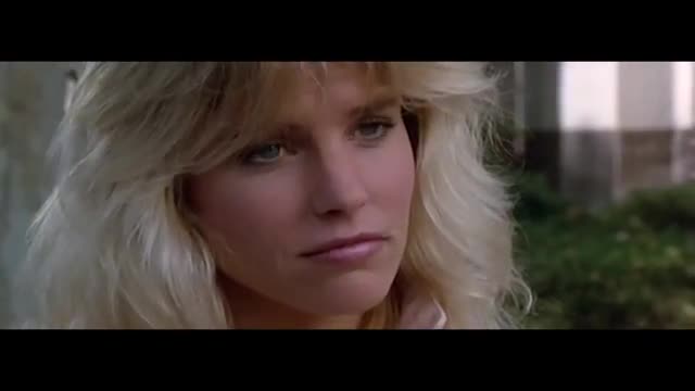 A woman with blonde hair turns her head, her blue eyes looking off to the side. The backdrop is a blurred green and white, suggesting an outdoor setting.