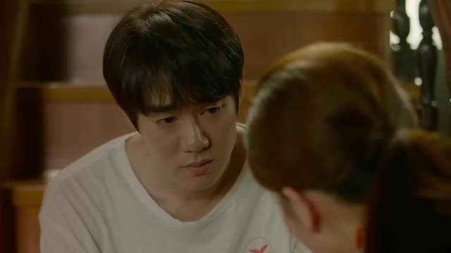 A man in a white t-shirt leans in, his gaze fixed on a woman whose head is turned away. The warm lighting suggests an intimate moment shared between them.