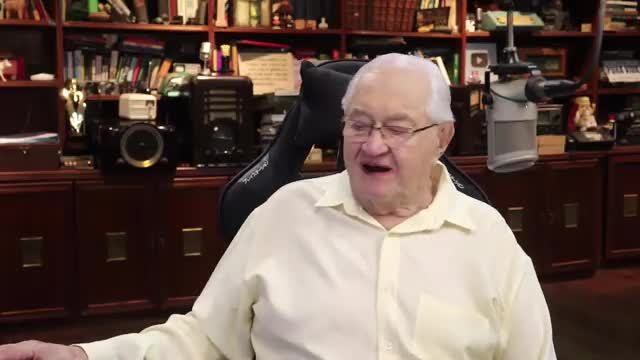 The man in the pale yellow shirt is speaking into a microphone, his mouth open wide. Behind him, shelves overflow with books and equipment, a typical setup for a Rede SPTV broadcast from Brazil.