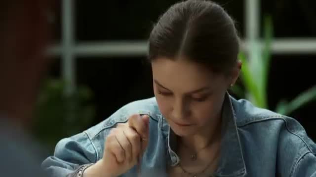 A young woman in a denim jacket stirs her drink with a spoon. Her gaze is focused downwards, as if lost in thought.