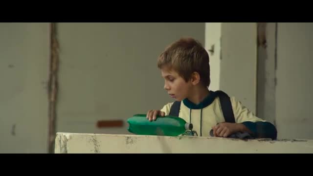 A young boy in a yellow and blue shirt leans over a concrete ledge, his hand resting on a green plastic bottle. He's looking down intently, as if contemplating something important. A young boy in a yellow and blue shirt leans over a concrete ledge, his hand resting on a green plastic bottle. He's looking down intently, as if contemplating something important.