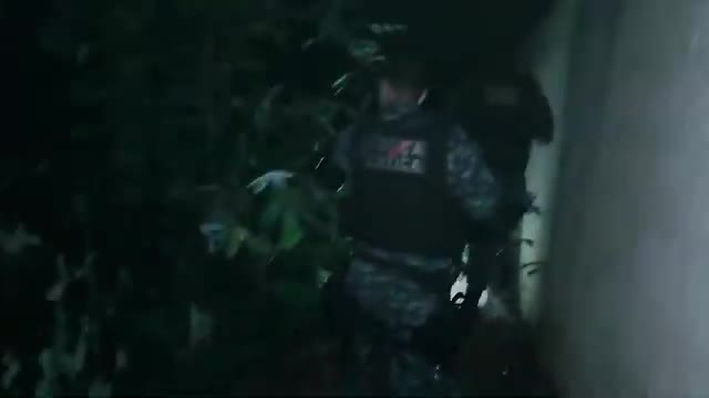 A man in tactical gear, likely from Rede SPTV, moves through thick foliage. The camera captures him from the side as he navigates the dense undergrowth.