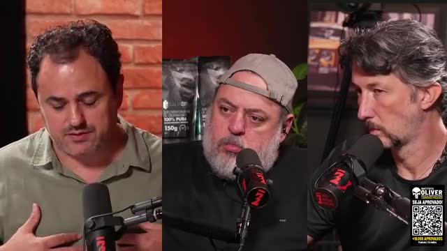 Three men are speaking into microphones, their faces illuminated by studio lights. The man on the left gestures with his hands while the other two listen intently.