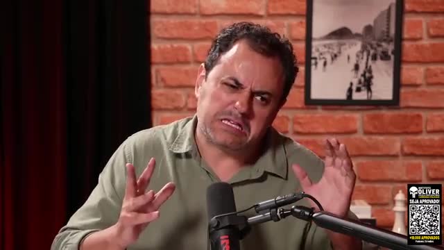 The man gestures emphatically, his brow furrowed in a way that suggests he's making a strong point. Behind him, a black and white photograph captures a bustling Brazilian beach scene.
