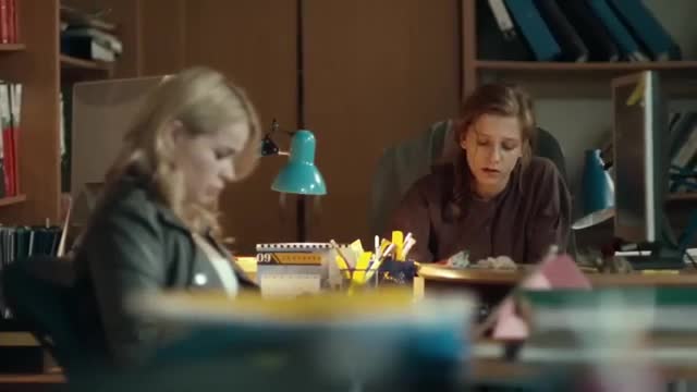 Two women are working at desks in an office. A bright blue lamp illuminates their workspace.