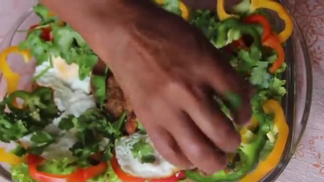 A hand carefully places green leaves onto a colorful salad. SPTV's broadcast continues as the dish, a vibrant mix of peppers and eggs, is finished.