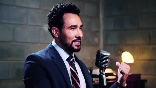 A man in a suit speaks into a vintage microphone, his hand gesturing towards a warm, glowing light. He's in a studio, likely for a Rede SPTV broadcast.