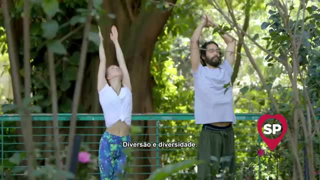 A woman and a man stand with their arms raised, palms together, in a park setting. The Rede SPTV logo appears in the lower right corner.