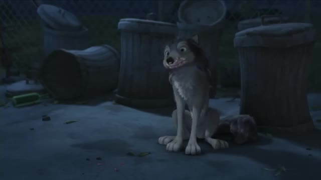 A grey wolf sits alertly next to a tipped-over trash can, its mouth slightly open. Another wolf lies curled up at its feet, partially obscured by shadow.