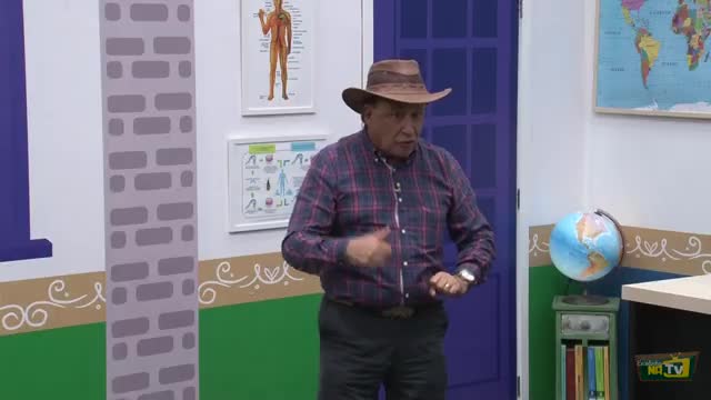 A man in a cowboy hat gestures with his hands while speaking, his plaid shirt a vibrant splash against the backdrop of a classroom setting. He's on Rede SPTV, likely explaining something with animated enthusiasm.
