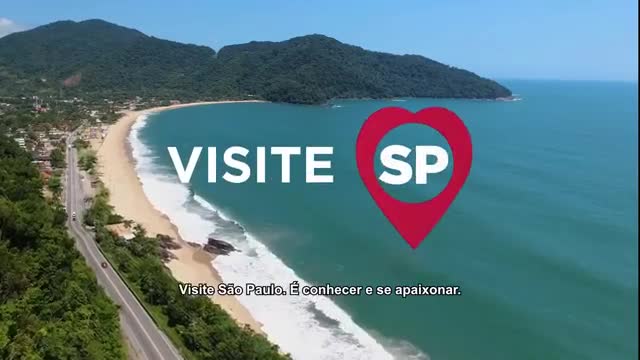 Cars drive along a coastal road beside a wide, sandy beach. The turquoise ocean meets the shore with gentle waves.