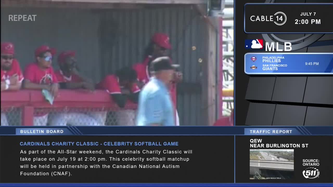From Cable 14 Hamilton, the Cardinals' dugout is visible, with players in red shirts and caps. A man in a light blue shirt walks in front of the dugout, while the bulletin board announces a celebrity softball game in partnership with the Canadian National Autism Foundation.
