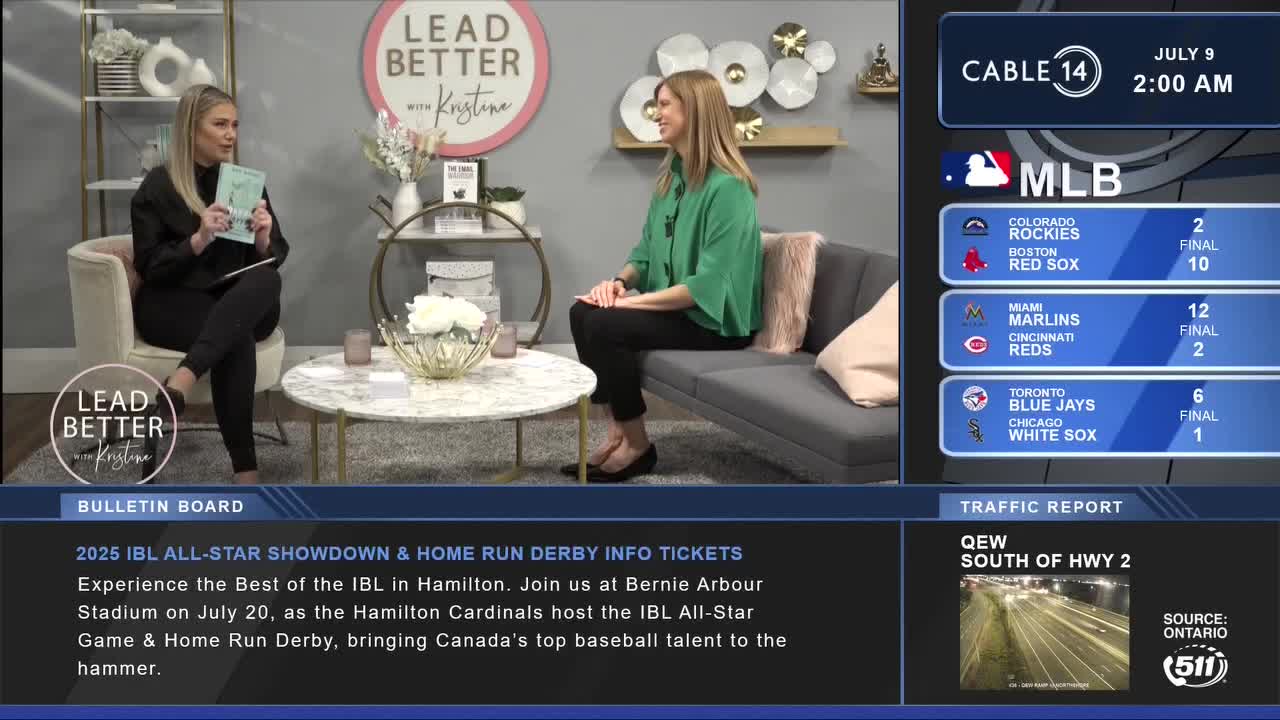 Two women are seated on a set, one holding a book, the other smiling. Cable 14 Hamilton is broadcasting, with baseball scores and a traffic report displayed on the screen.
