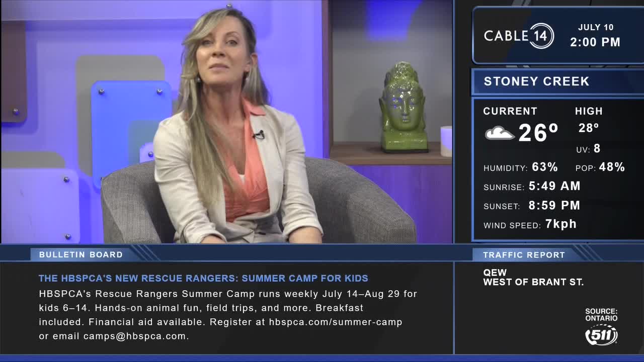 On Cable 14 Hamilton, a woman in a blazer sits in a studio chair, speaking to the camera. The local weather report for Stoney Creek shows a sunny 26 degrees Celsius.
