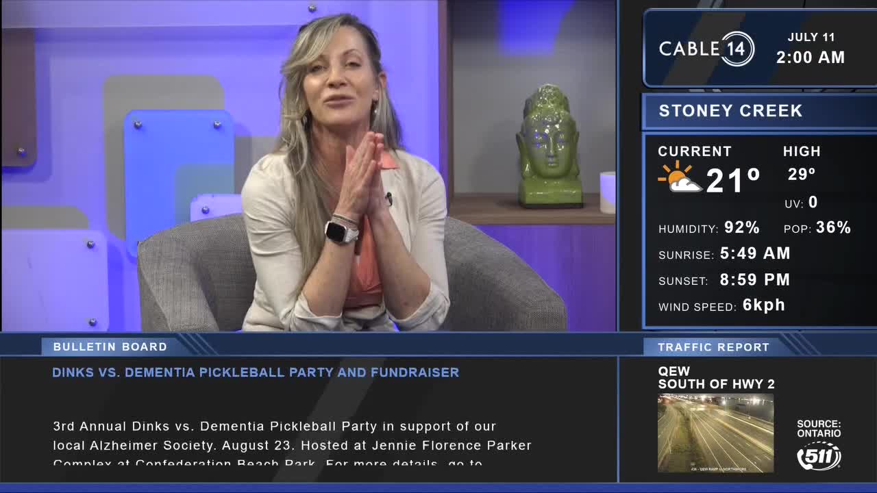 The woman, seated in a studio, gestures with her hands as she speaks. The Cable 14 Hamilton broadcast shows local weather and a traffic report from the QEW.
