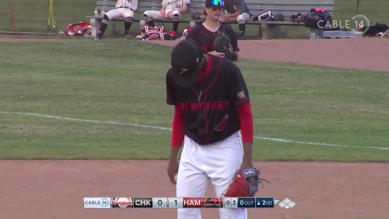 The pitcher, in a black and red uniform, is looking down, holding his glove. Cable 14 Hamilton is broadcasting the game, and the scoreboard shows the second inning underway.

