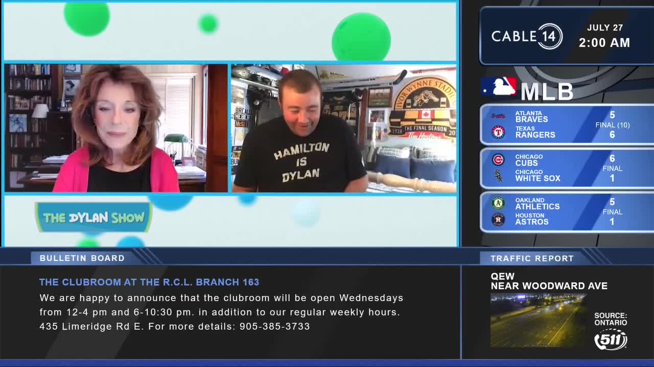 It's 2:00 AM on Cable 14, and the "Dylan Show" is on. A woman in a pink jacket and a man in a "Hamilton is Dylan" t-shirt are on screen, with MLB scores and local traffic updates displayed.

