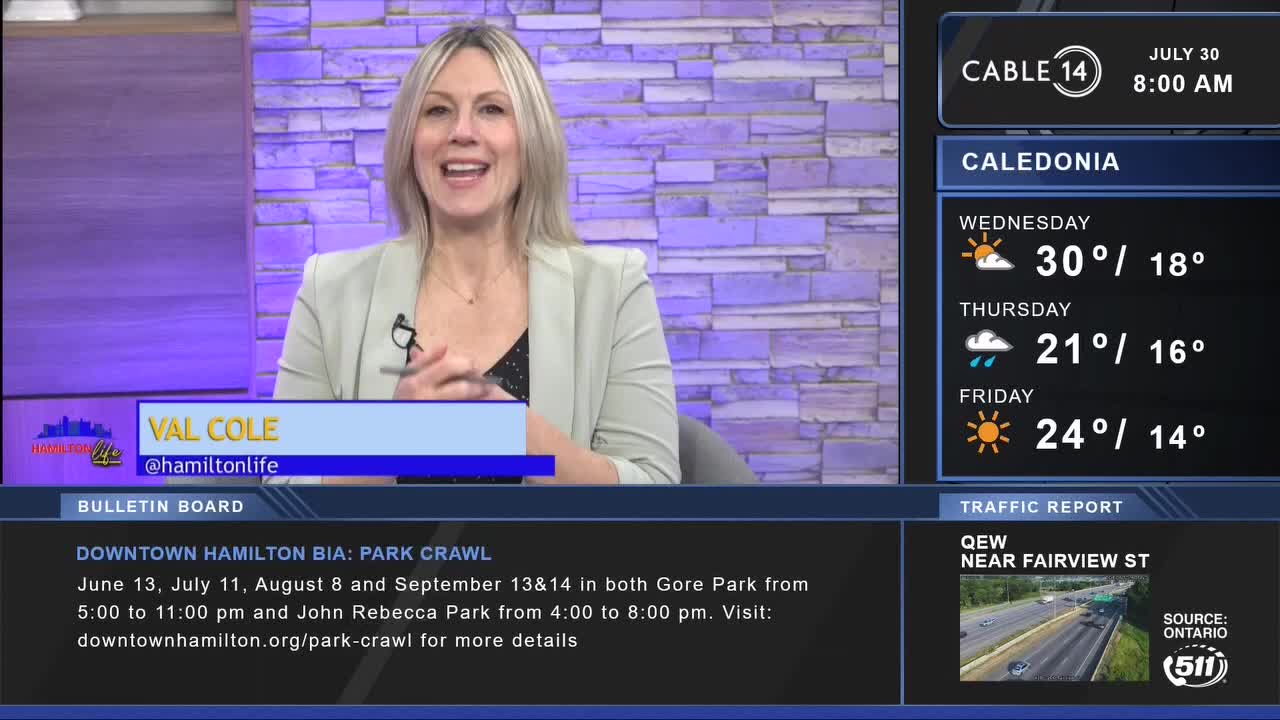 Val Cole from Cable 14 Hamilton is smiling, likely mid-broadcast, with weather and traffic information displayed beside her. The bulletin board announces a park crawl in downtown Hamilton.
