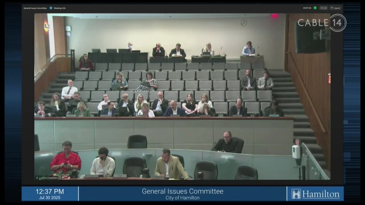 A meeting of the General Issues Committee in Hamilton, Canada, is underway, as seen on Cable 14. The camera angle is wide, capturing rows of people seated in a tiered room.

