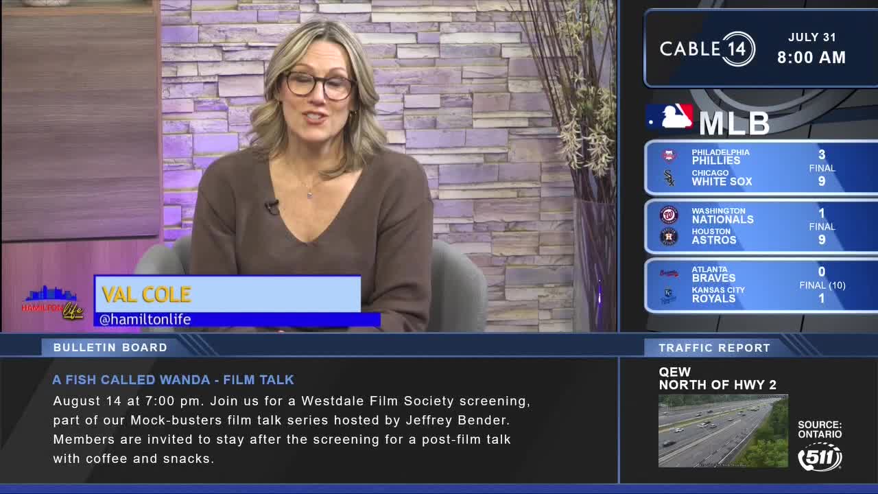 Val Cole from Cable 14 Hamilton is speaking, a graphic with baseball scores and traffic updates is beside her. The bulletin board advertises a film talk, and the time is 8:00 AM.
