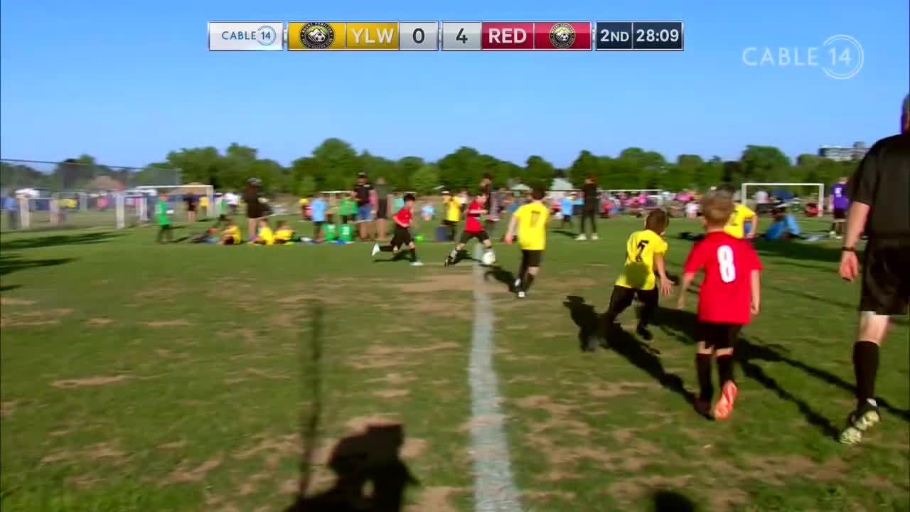 The Cable 14 broadcast shows a youth soccer match underway. A player in red, number 8, is running toward the ball, with the score showing Yellow 0, Red 4.
