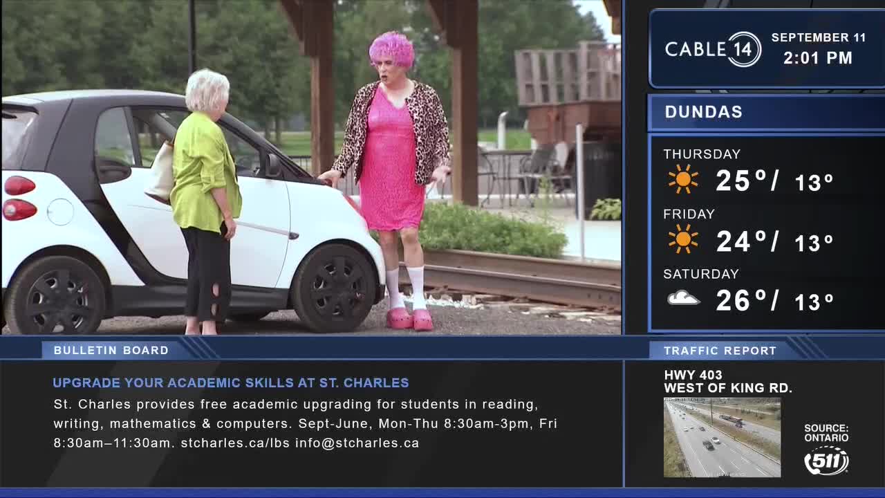 A person in a pink dress and a leopard-print jacket stands next to a small white car, talking animatedly to another person. Cable 14 Hamilton's weather report for Dundas is displayed, with temperatures in the mid-twenties.
