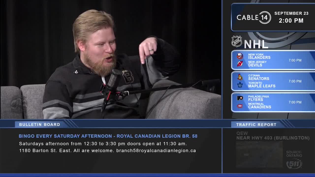 A man with a beard gestures emphatically toward something off-screen, his mouth open as if speaking on Cable 14 in Hamilton. Beside him, a graphic displays NHL game times, and a bulletin board advertises bingo at the Royal Canadian Legion.
