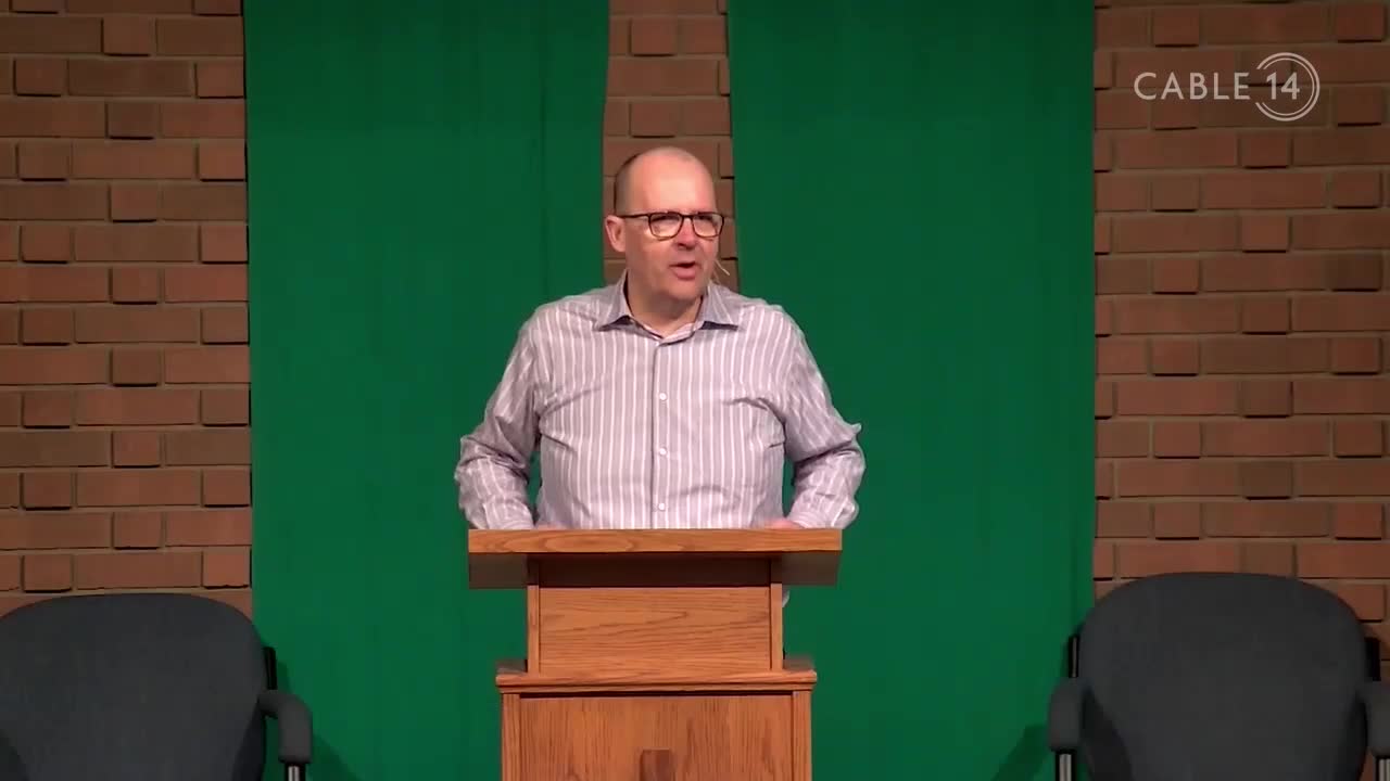 A man in a striped shirt speaks from behind a wooden podium, likely on Cable 14 in Hamilton, Canada. The backdrop features a brick wall and a green screen, with the station's logo in the corner.
A man in a striped shirt speaks from behind a wooden podium, likely on Cable 14 in Hamilton, Canada. The backdrop features a brick wall and a green screen, with the station's logo in the corner.